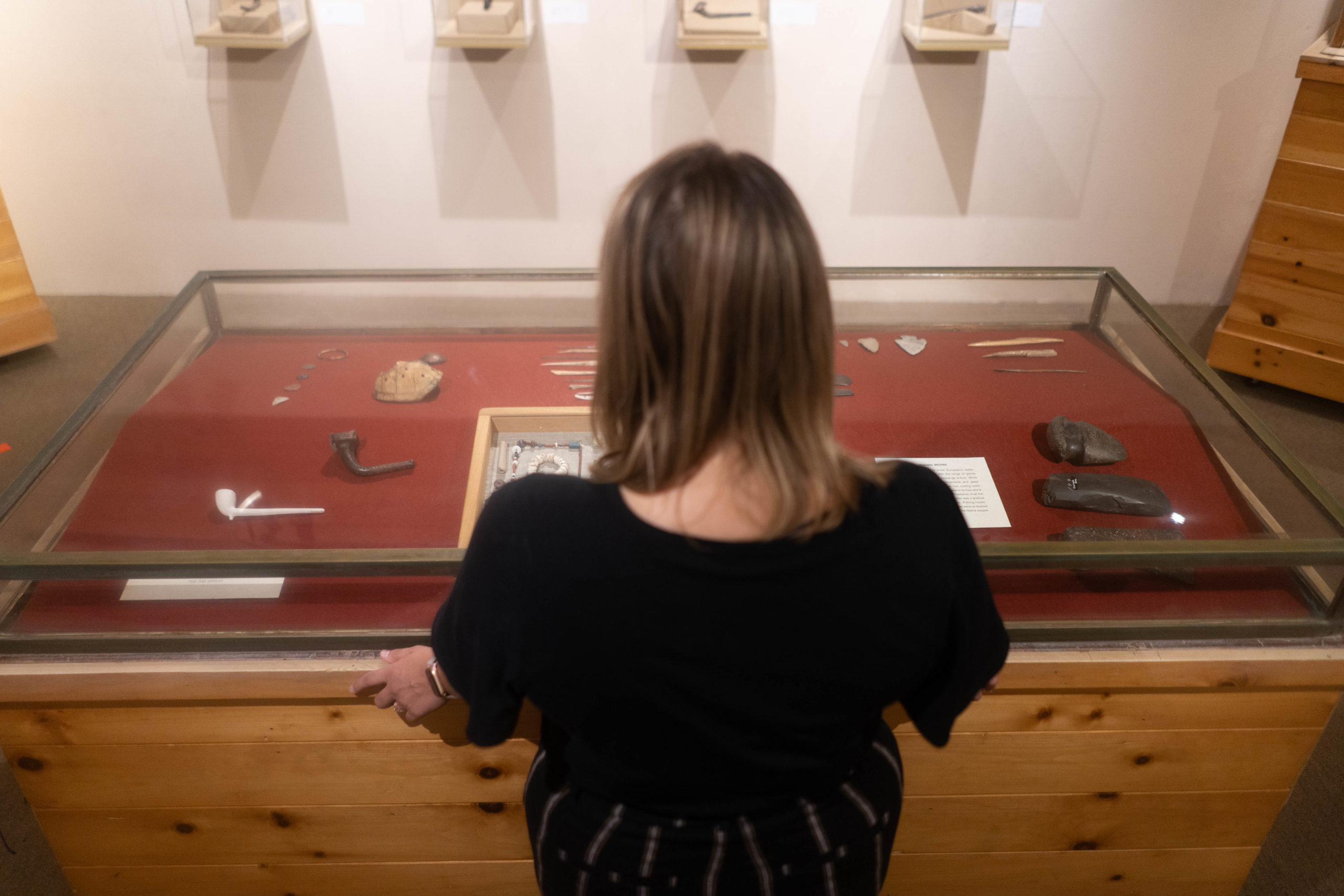 Woman observing indigenous artifacts through enclosed class case