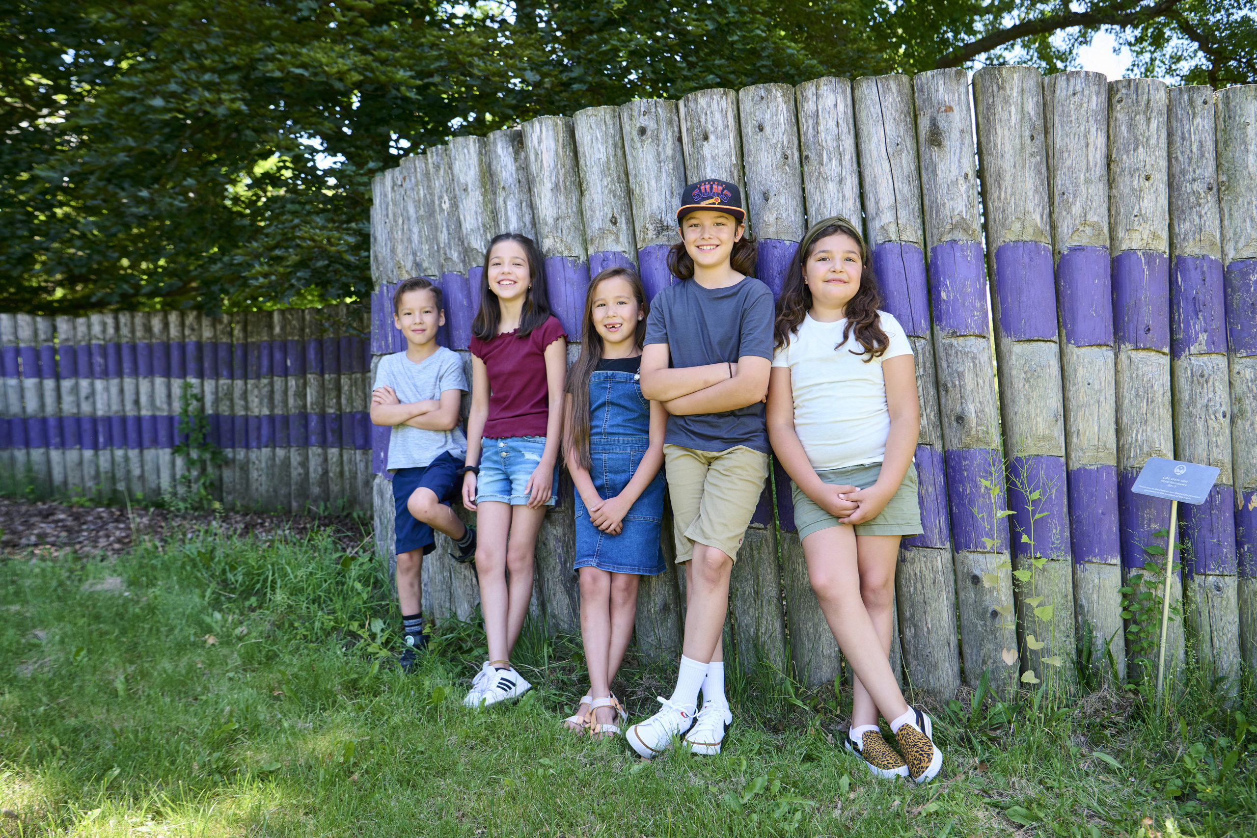 Five children leaning against wooden fence outside